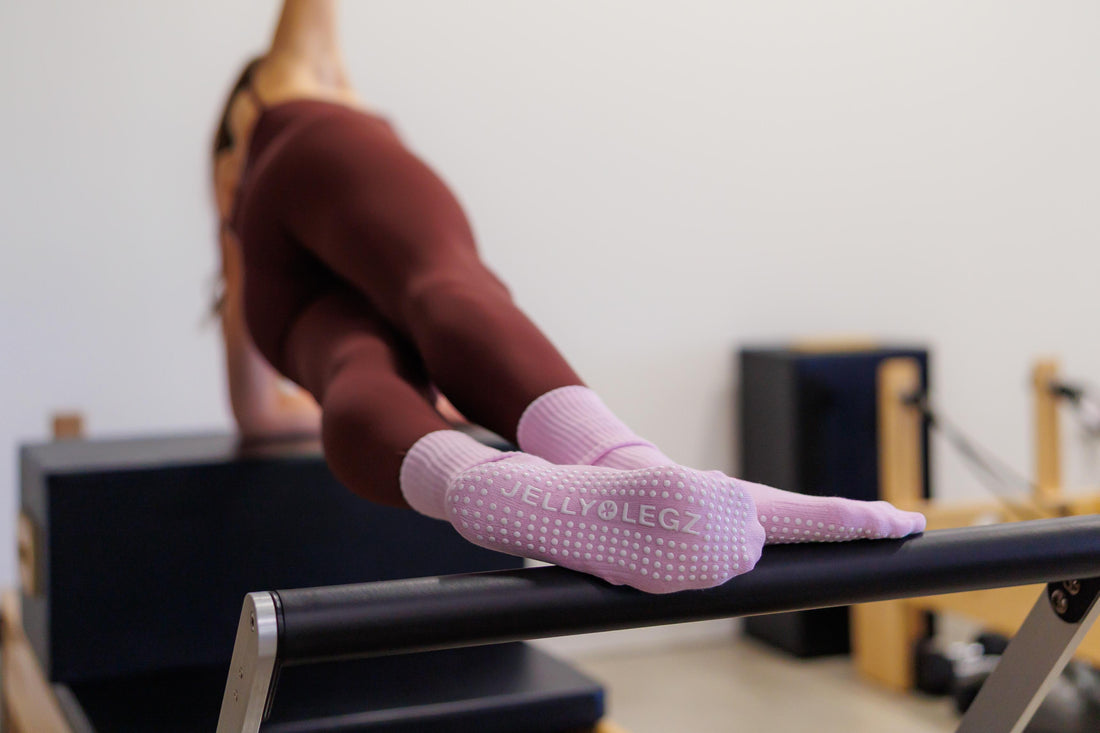 Woman wearing JellyLegz black Pilates grip socks during reformer workout in bright studio